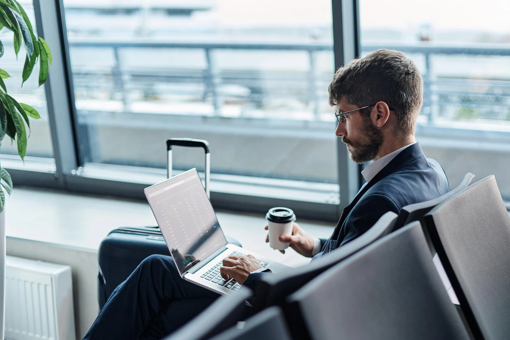 Persona trabajando con notebook y café en la sala de espera del aeropuerto.